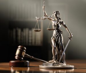 Statue of Lady Justice balancing scales and holding a sword on a courthouse desk with a gavel nearby.